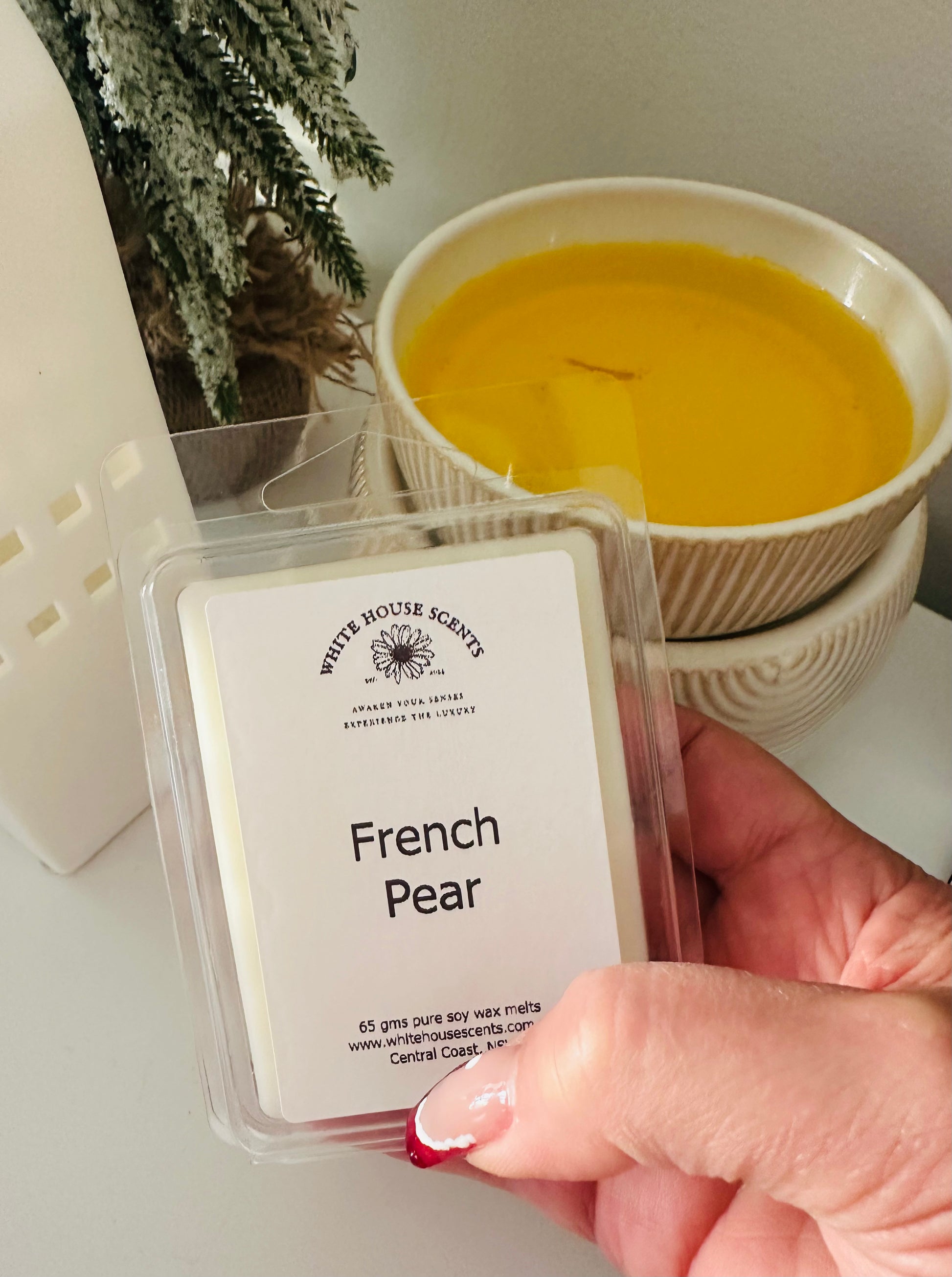 Hand holding a wax melt labeled 'French Pear' with a candle in the background.