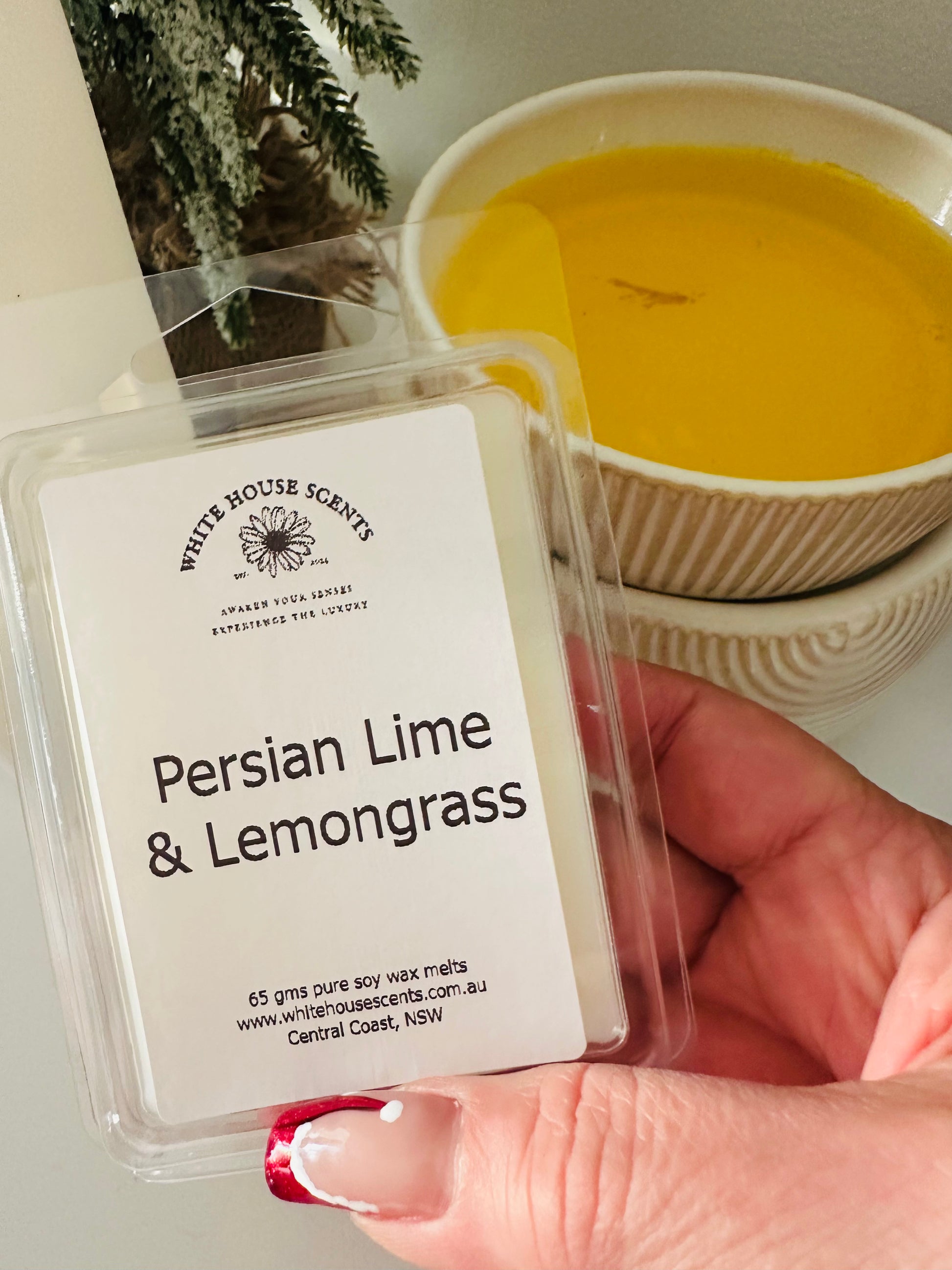 White House Scents wax melt labeled 'Persian Lime & Lemongrass' held by a hand with a blurred candle in the background.
