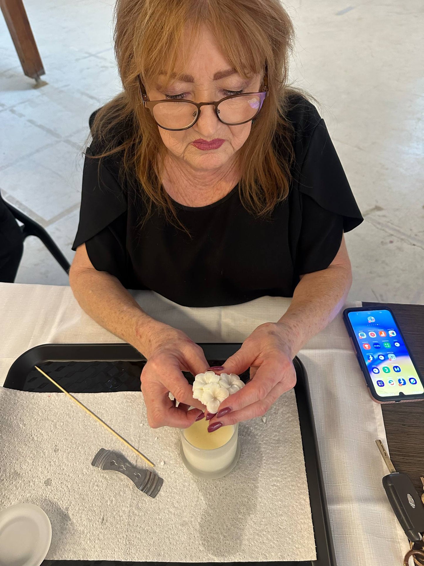 Woman making a candle at a table with a phone and tools on the side.