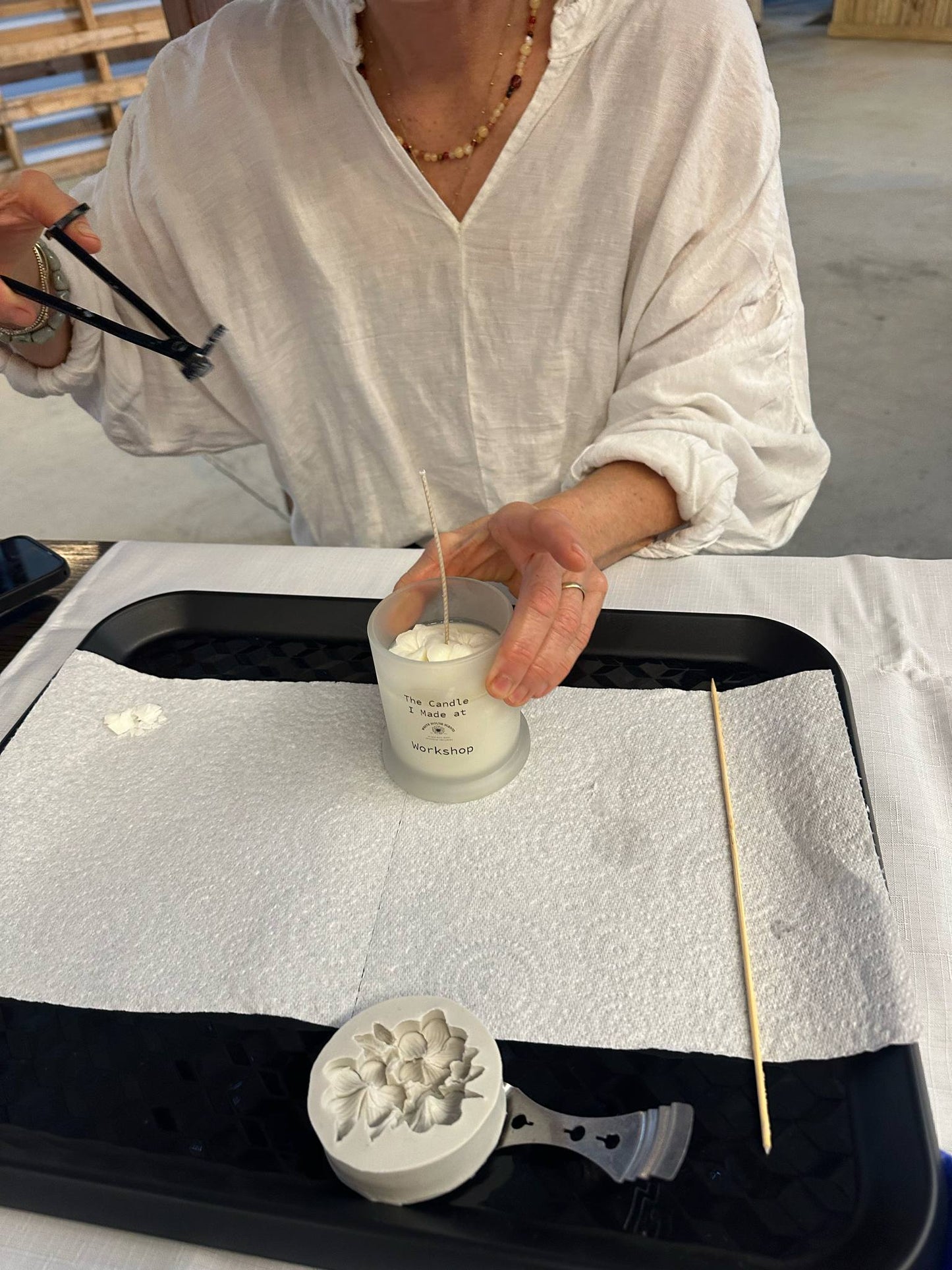 Person holding a small glass container with a candle on a white surface with a black tray.