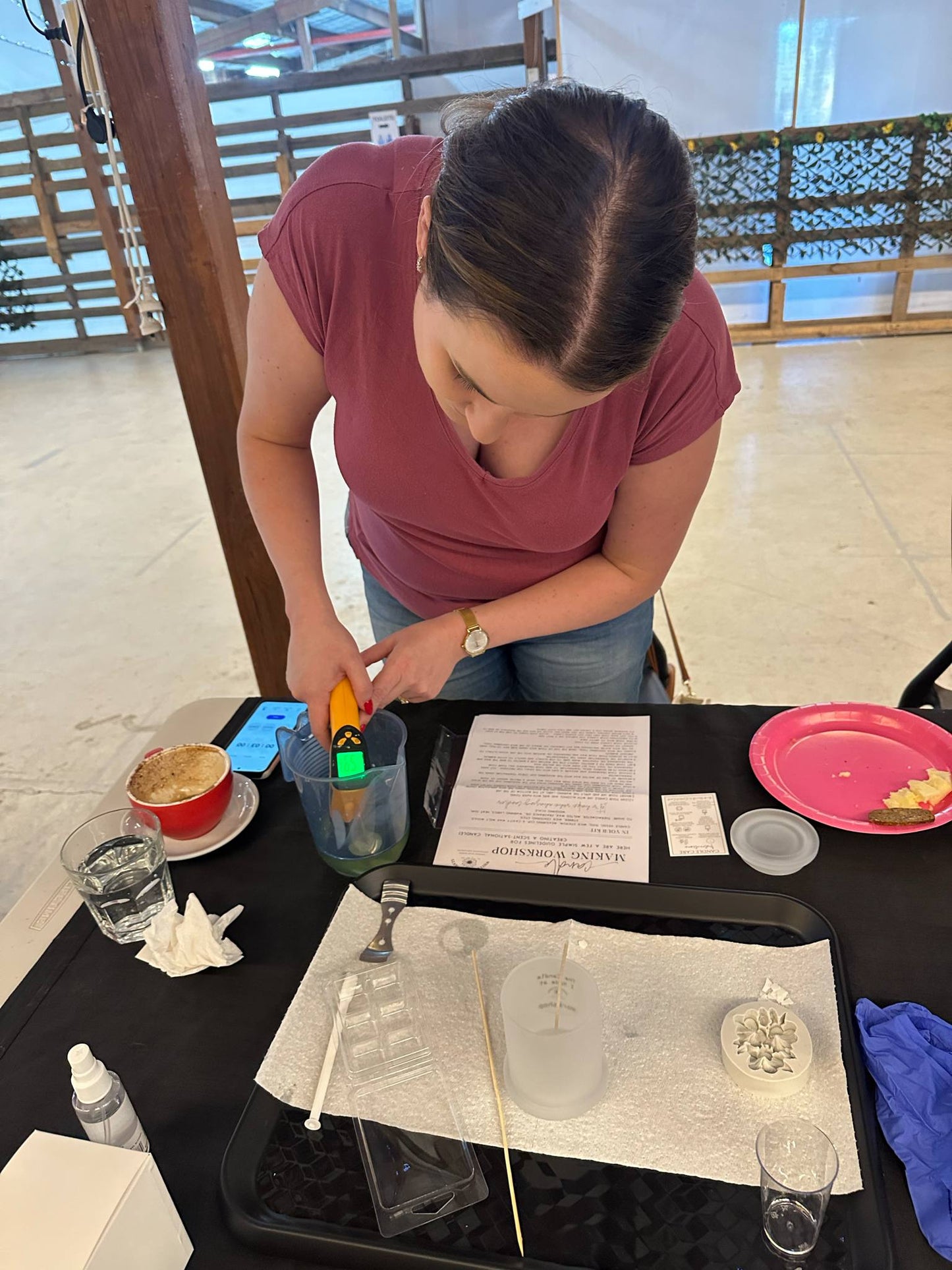 Person using a digital thermometer at a table with various items including a smartphone and making candle